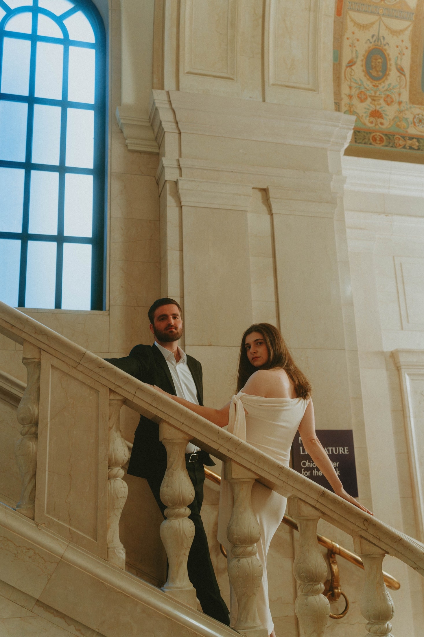 Tylar and Carly descending a wide marble staircase hand in hand