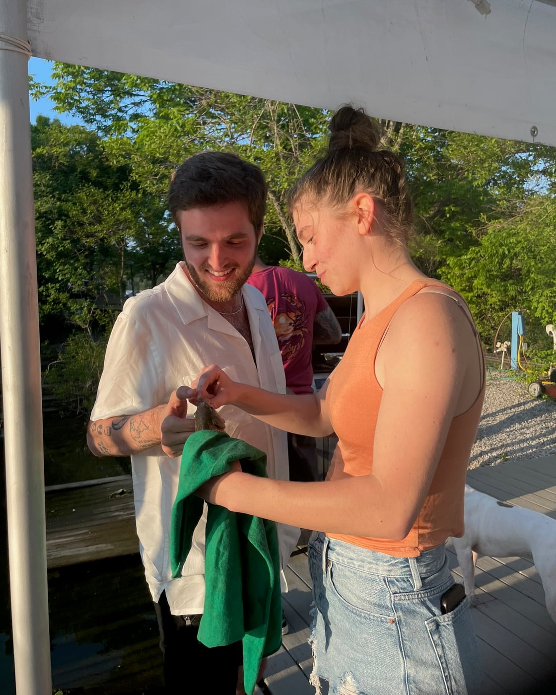 Tylar handing Carly a jacket on a deck by the water