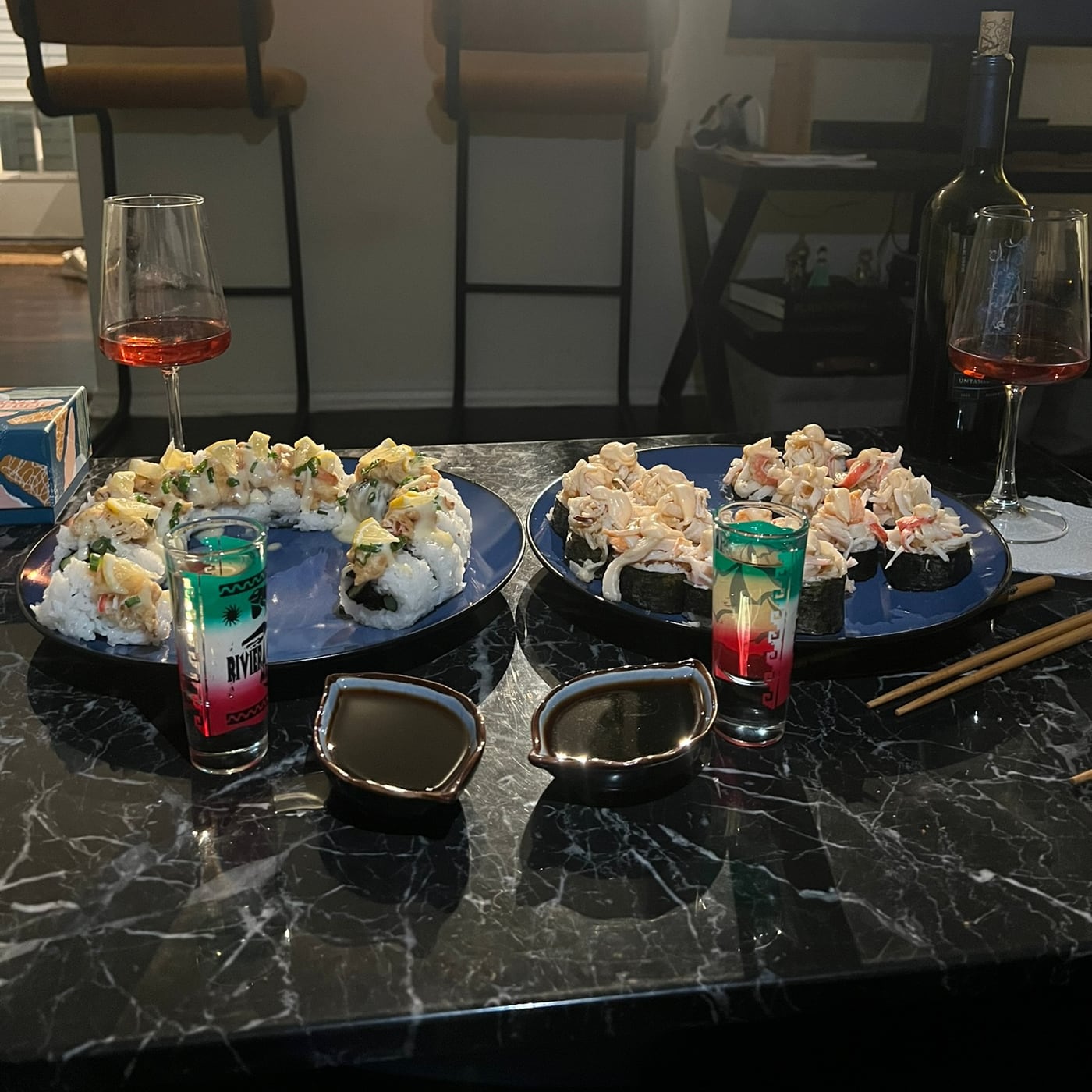 Homemade sushi plated on the counter beside two glasses of wine