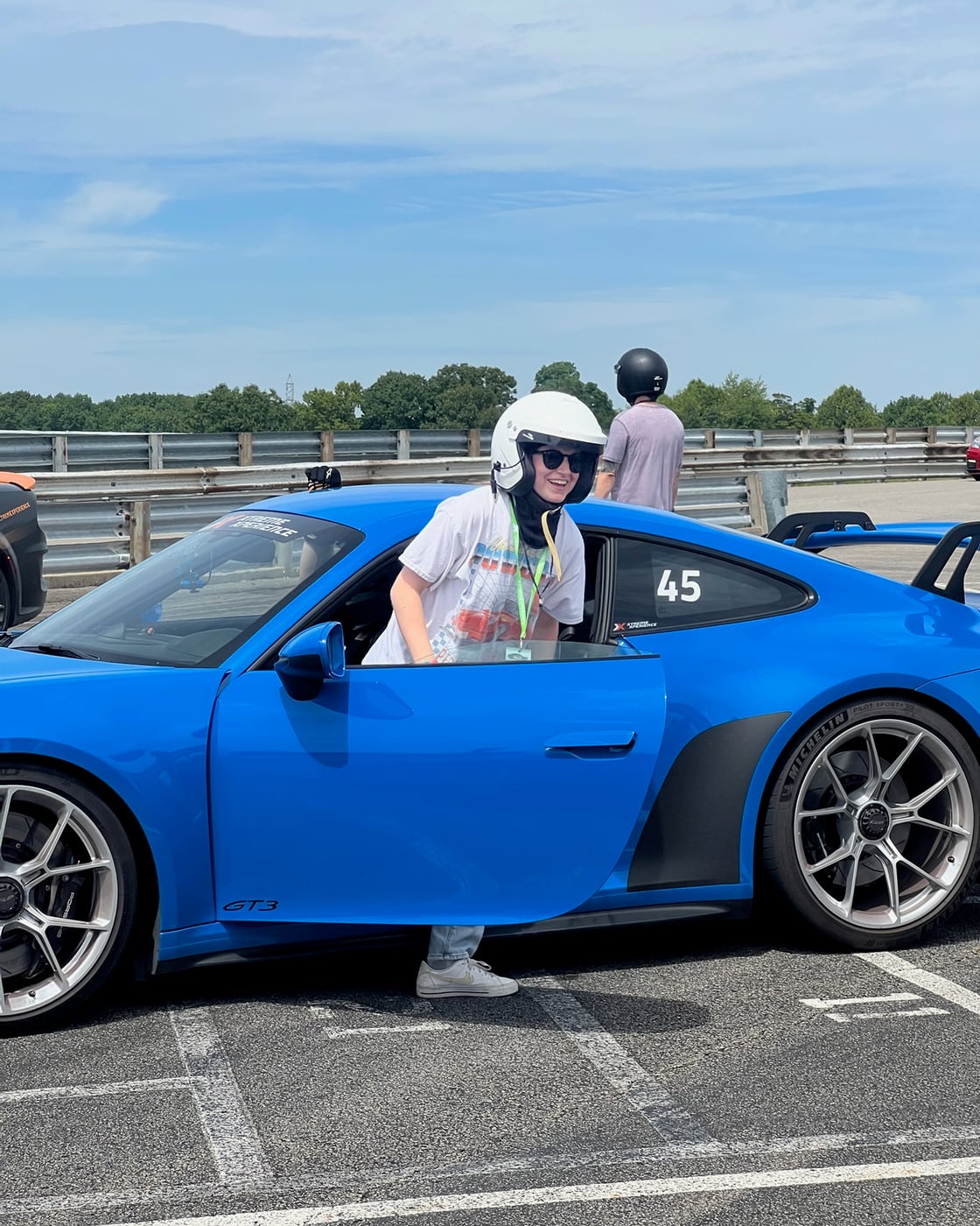Carly in a helmet behind the wheel of a blue sports car