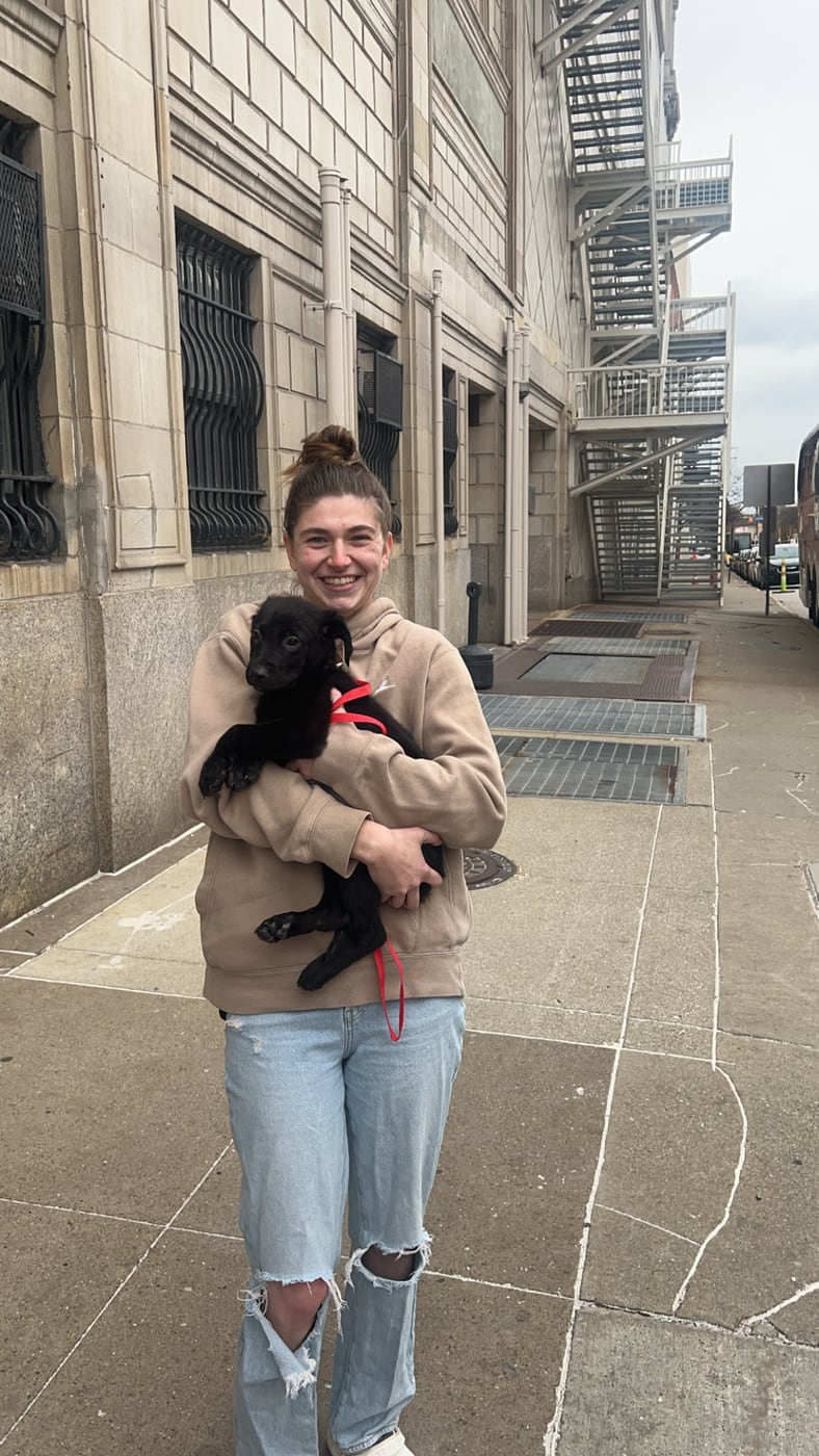 Carly holding a black puppy on a city sidewalk
