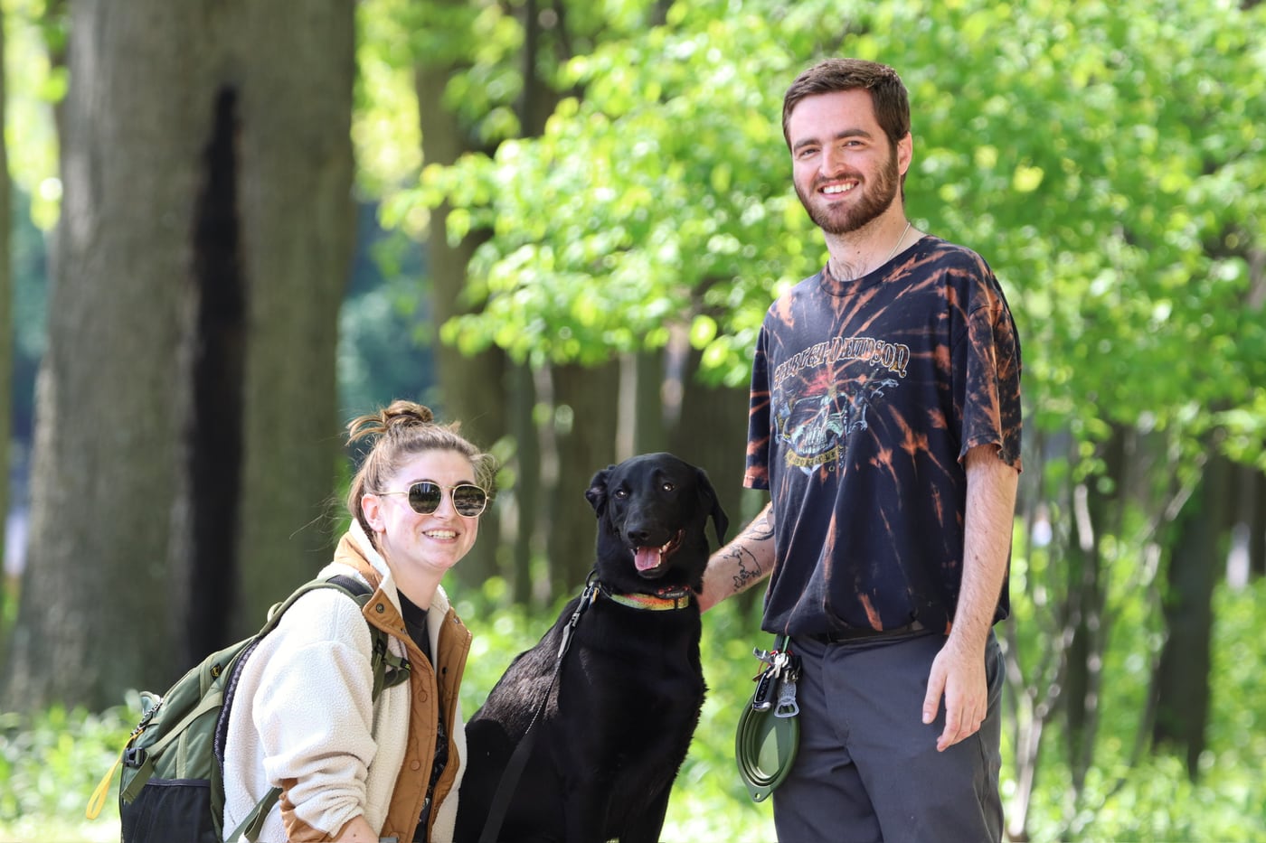 Tylar and Carly walking a black dog along a wooded trail