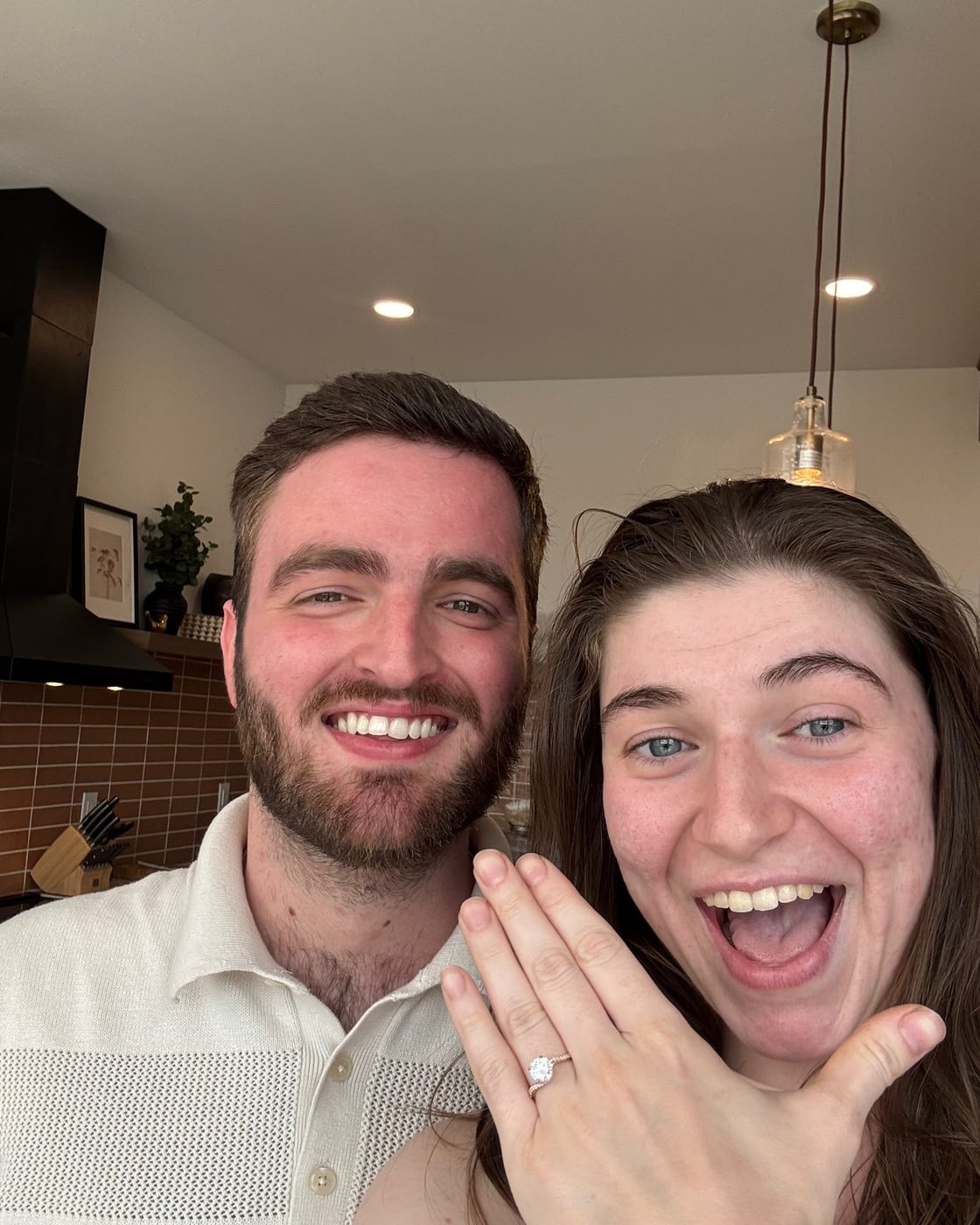 Carly showing her engagement ring, both of them beaming
