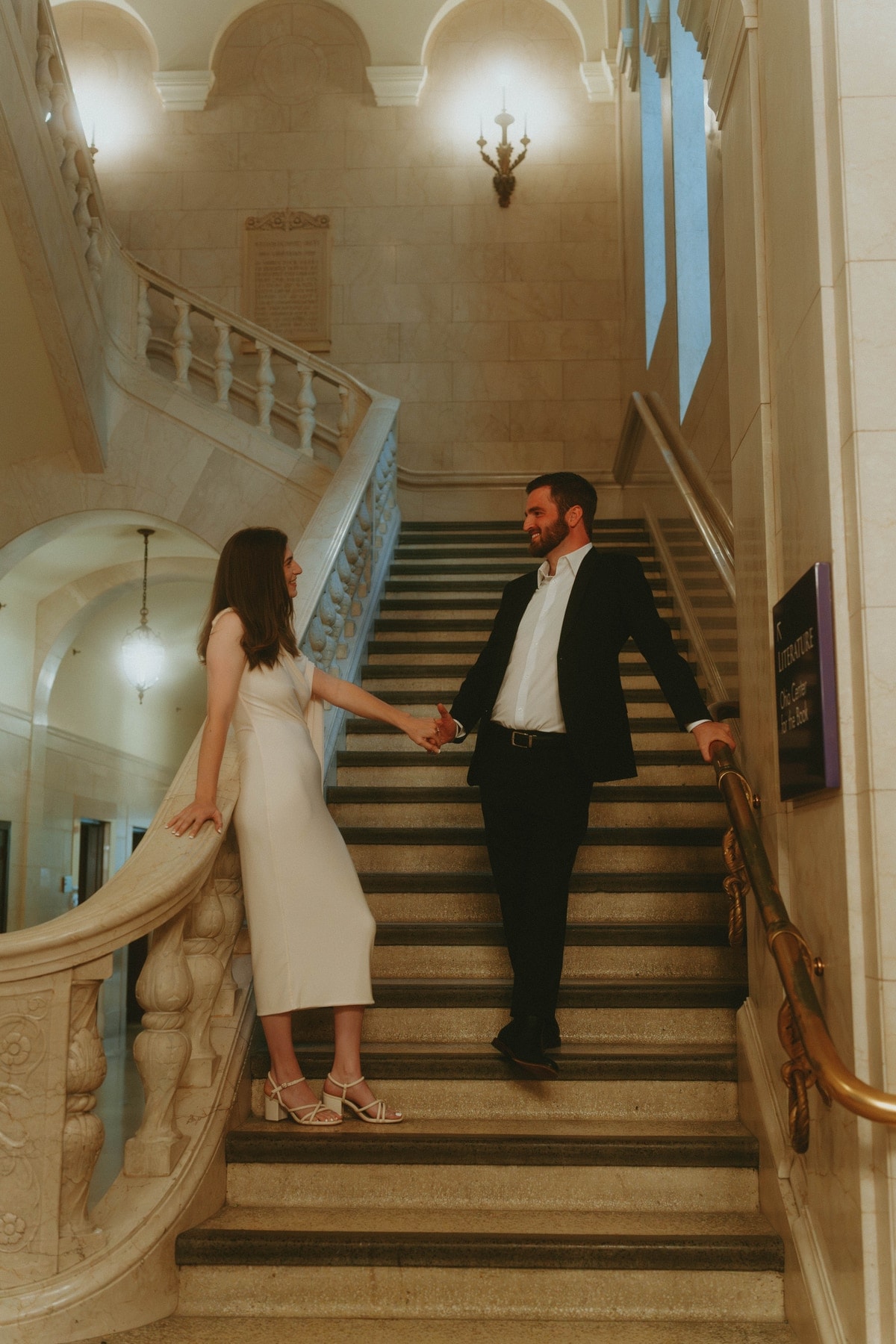 Tylar and Carly holding hands on a marble staircase