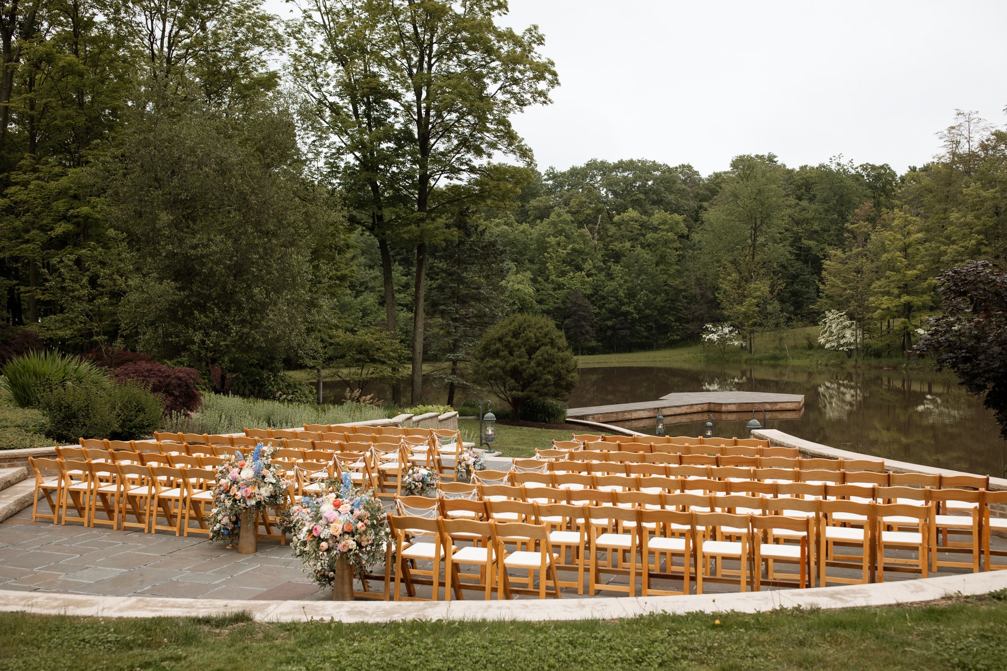 The stone ceremony amphitheater beside the pond, set with wooden chairs and florals